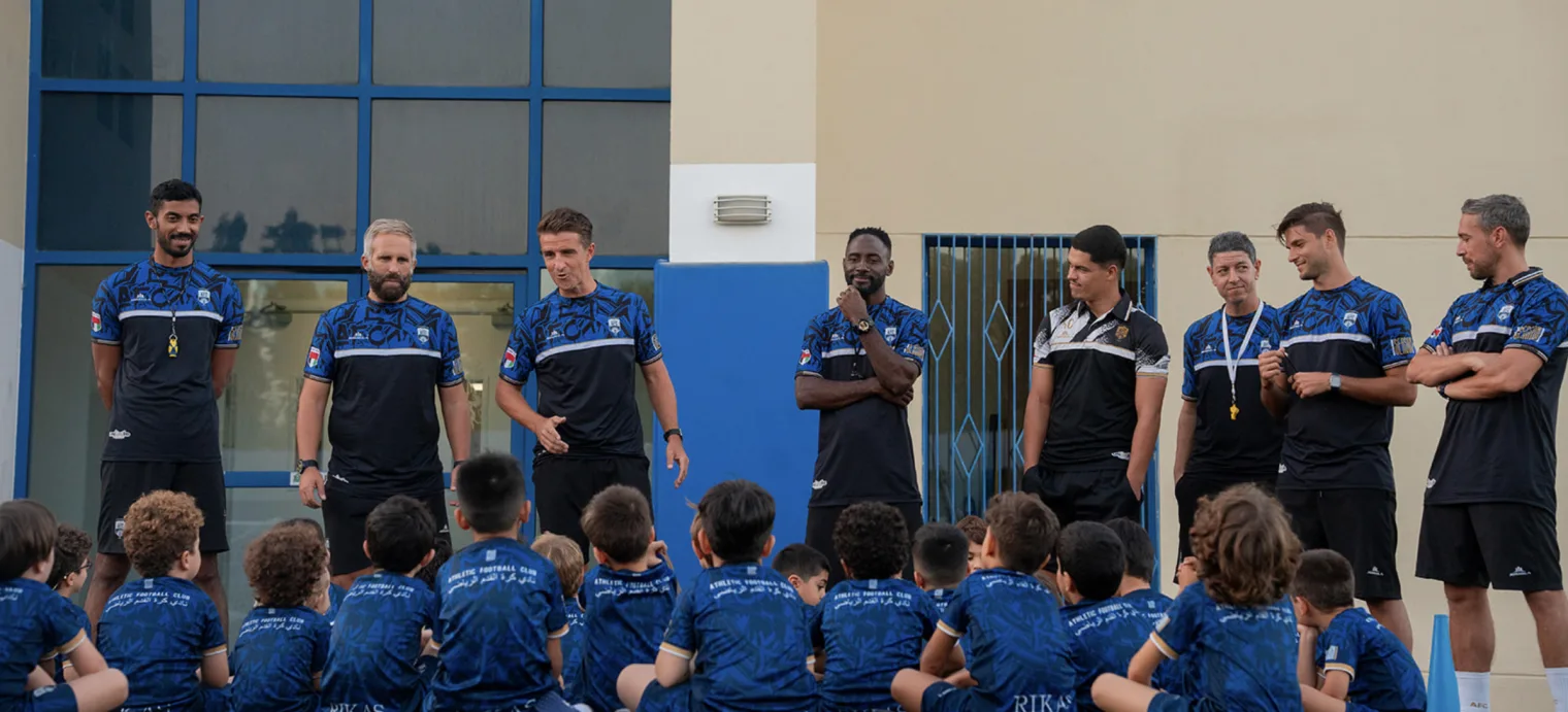 The AFC coaching staff standing in front of a group of seated young players