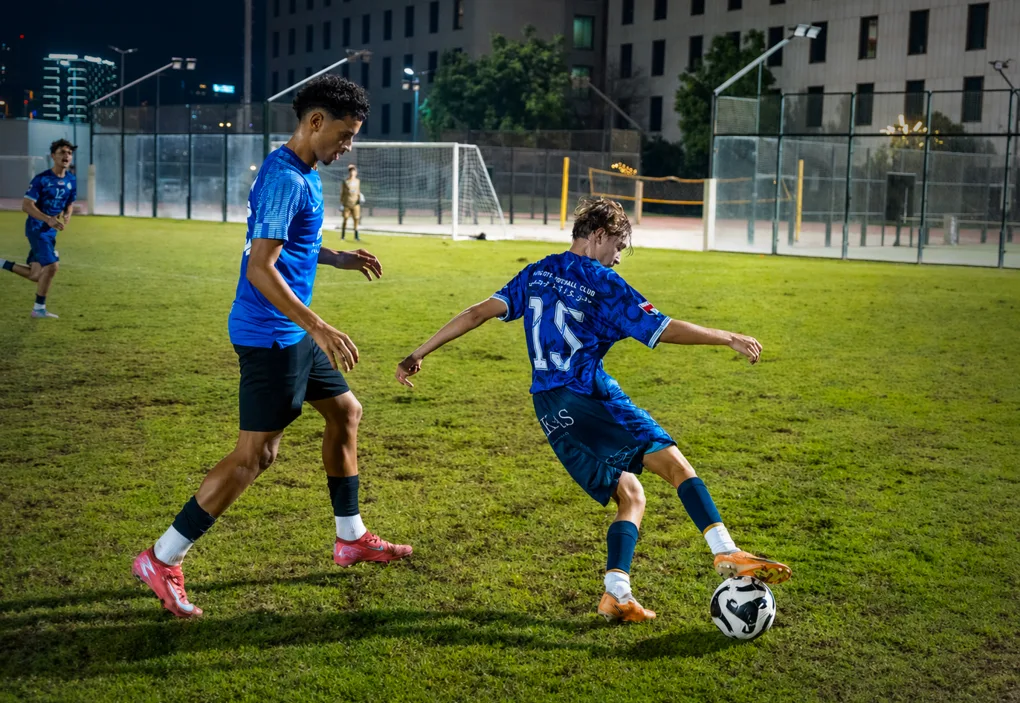 Two AFC players contesting the ball on a floodlit pitch at night